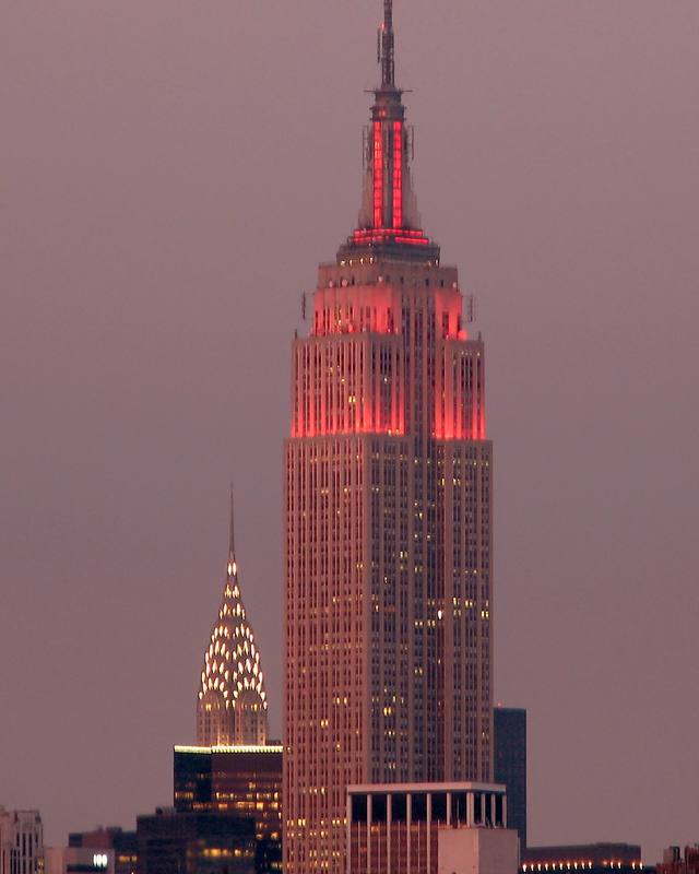 Empire State Building iluminado ao entardecer, com o Chrysler Building ao fundo, em Nova York