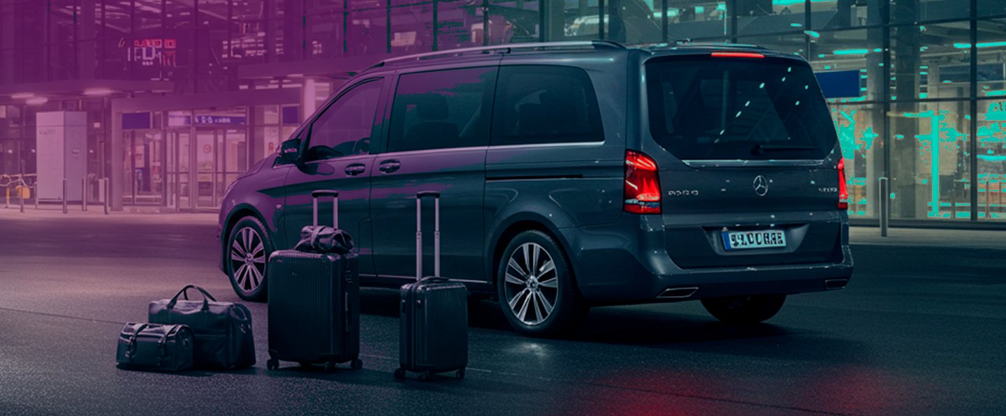 Van escura parada em frente ao terminal de um aeroporto à noite, com malas e uma mochila no chão ao lado da porta