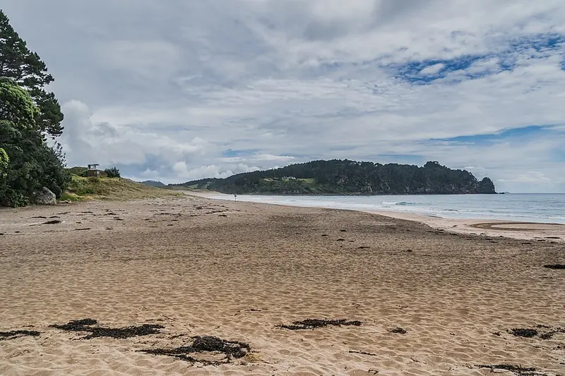 Faixa de areia dourada de Hot Water Beach com mar aberto na península de Coromandel